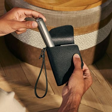 O mână scoate un dispozitiv Ploom AURA din husa Ploom  Jet Black
